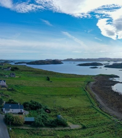 Aerial view of Spogan HQ, a croft house by the shore on the Isle of Lewis, surrounded by fields and the sea beyond